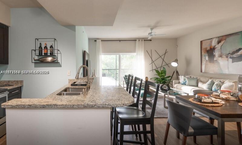 Kitchen featuring a breakfast bar, stone-finish countertops, stainless steel dual-basin sink, and dark cabinetry, with wood-finish flooring throughout