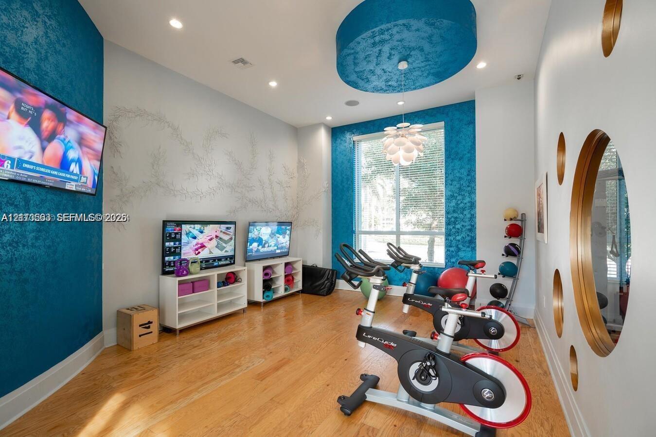 Room featuring wood-finish flooring, textured teal accent walls, a circular recessed ceiling detail with a tiered light fixture, large window, and wall-integrated circular glass accents