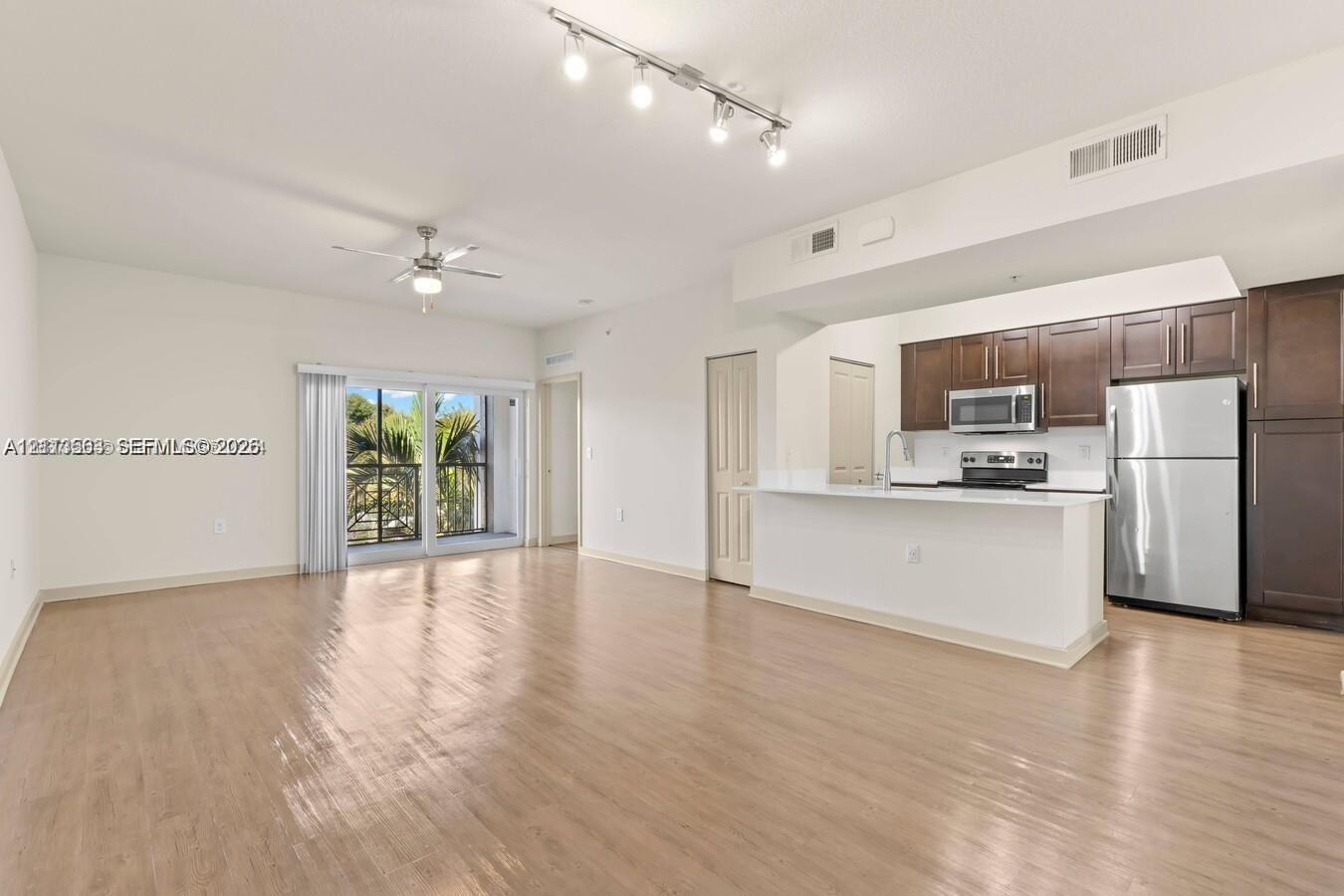 Open-concept interior featuring wood-finish flooring, a kitchen with dark cabinetry and stainless steel appliances, a breakfast bar, recessed track lighting, and a sliding glass door