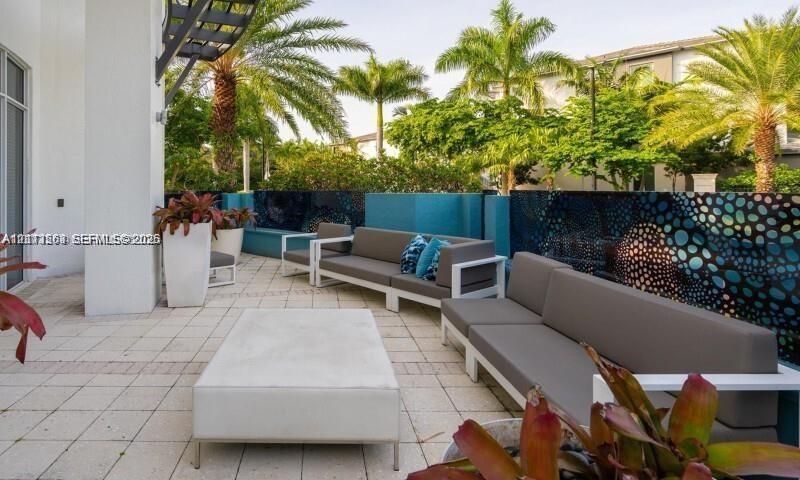 Outdoor terrace featuring paved stone flooring, decorative privacy screening with patterned accents, and perimeter landscaping with mature palm trees Outdoor terrace featuring paved stone flooring, decorative privacy screening with patterned accents, and perimeter landscaping with mature palm trees