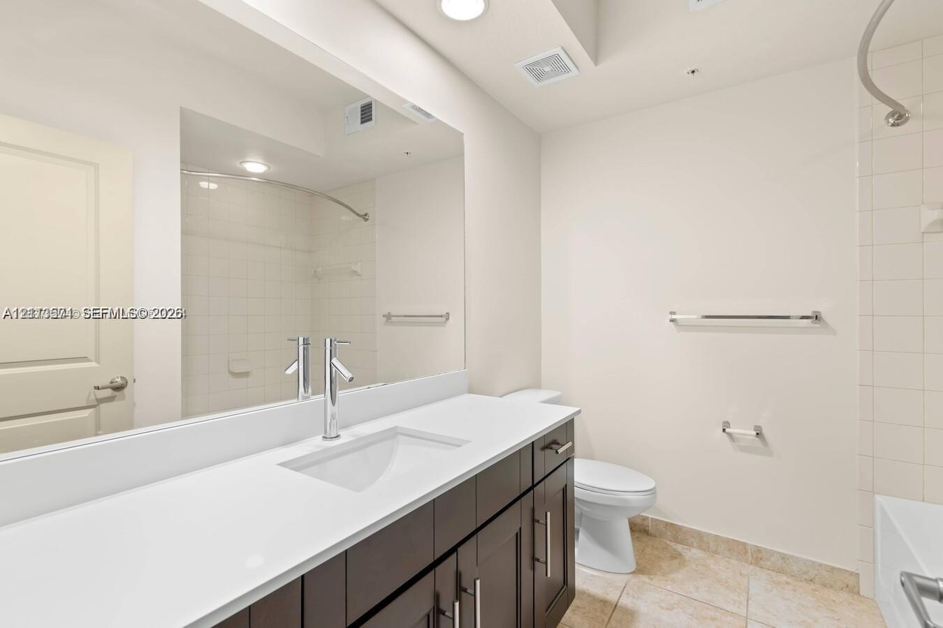 Bathroom featuring a dark-finish wood vanity, white countertop with an integrated rectangular basin, single-lever polished chrome faucet, full-width wall mirror, and tile flooring