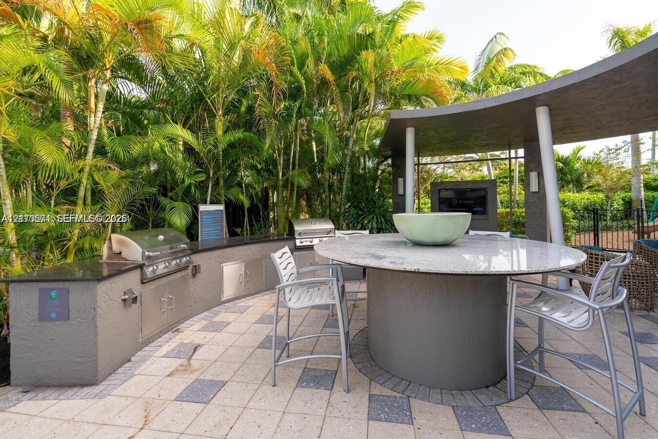 Outdoor kitchen featuring a built-in stainless steel grill, stone-surfaced prep counters, integrated cabinetry, a circular stone-topped island, and a covered patio structure