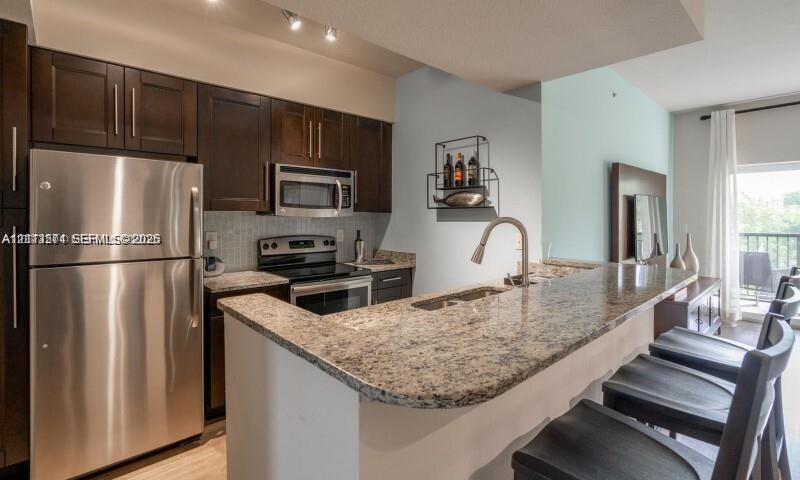 Kitchen featuring dark wood cabinetry, stone countertops, stainless steel appliances, breakfast bar, and undermount sink