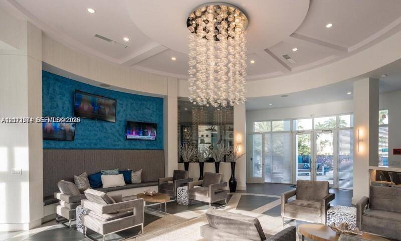 Circular rotunda ceiling featuring recessed lighting and a tiered glass-sphere chandelier, textured blue accent wall, polished stone flooring with geometric inlays, and floor-to-ceiling glass panel doors