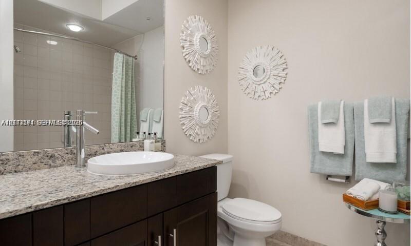 Dark wood-finish vanity with a stone countertop, vessel sink, polished chrome faucet, and full-wall mirror