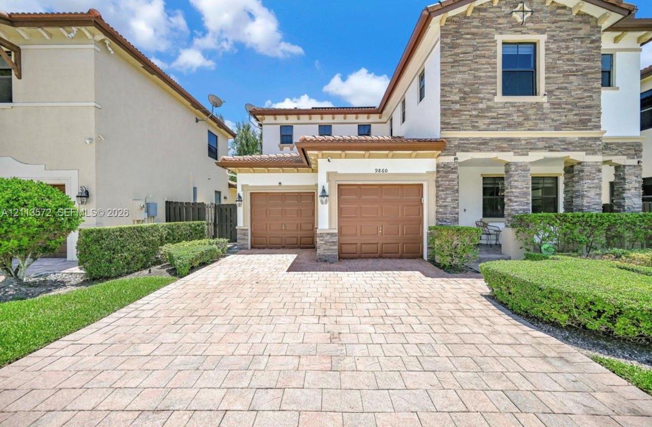 Two-story residence featuring a stone-veneer facade, paver driveway, three-car garage, tile roof, and manicured landscaping