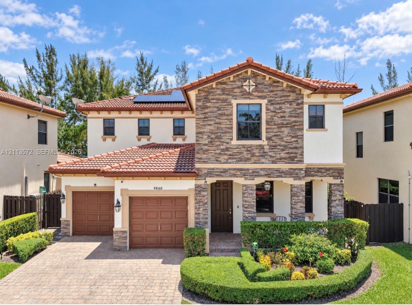 Two-story residence with a stone veneer facade, clay tile roof, dual-bay garage, solar panels, and a paver driveway