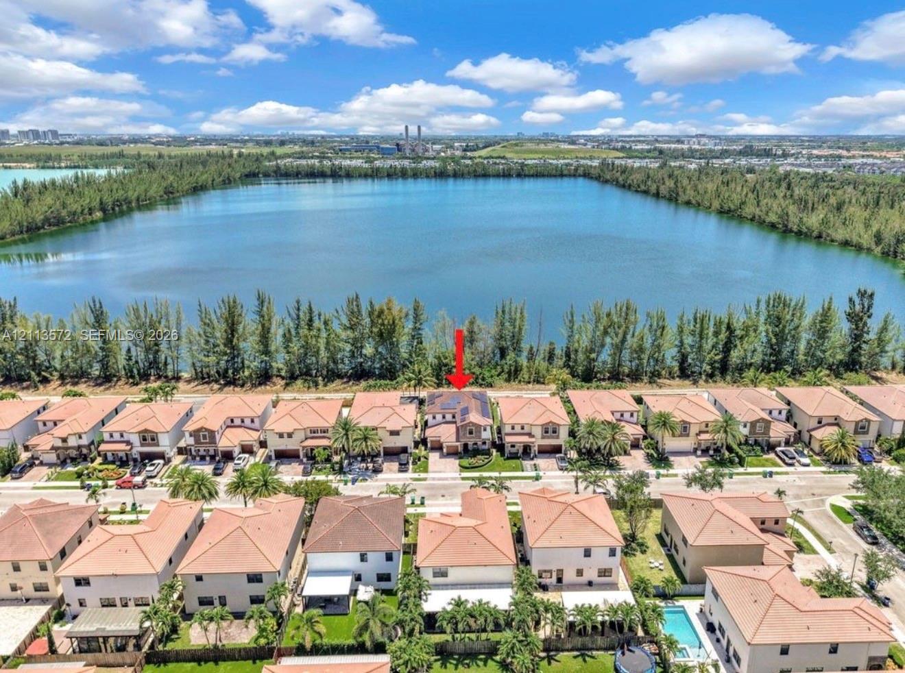 Aerial perspective featuring a two-story residence with a multi-hipped roof, positioned along a waterfront bordered by mature trees