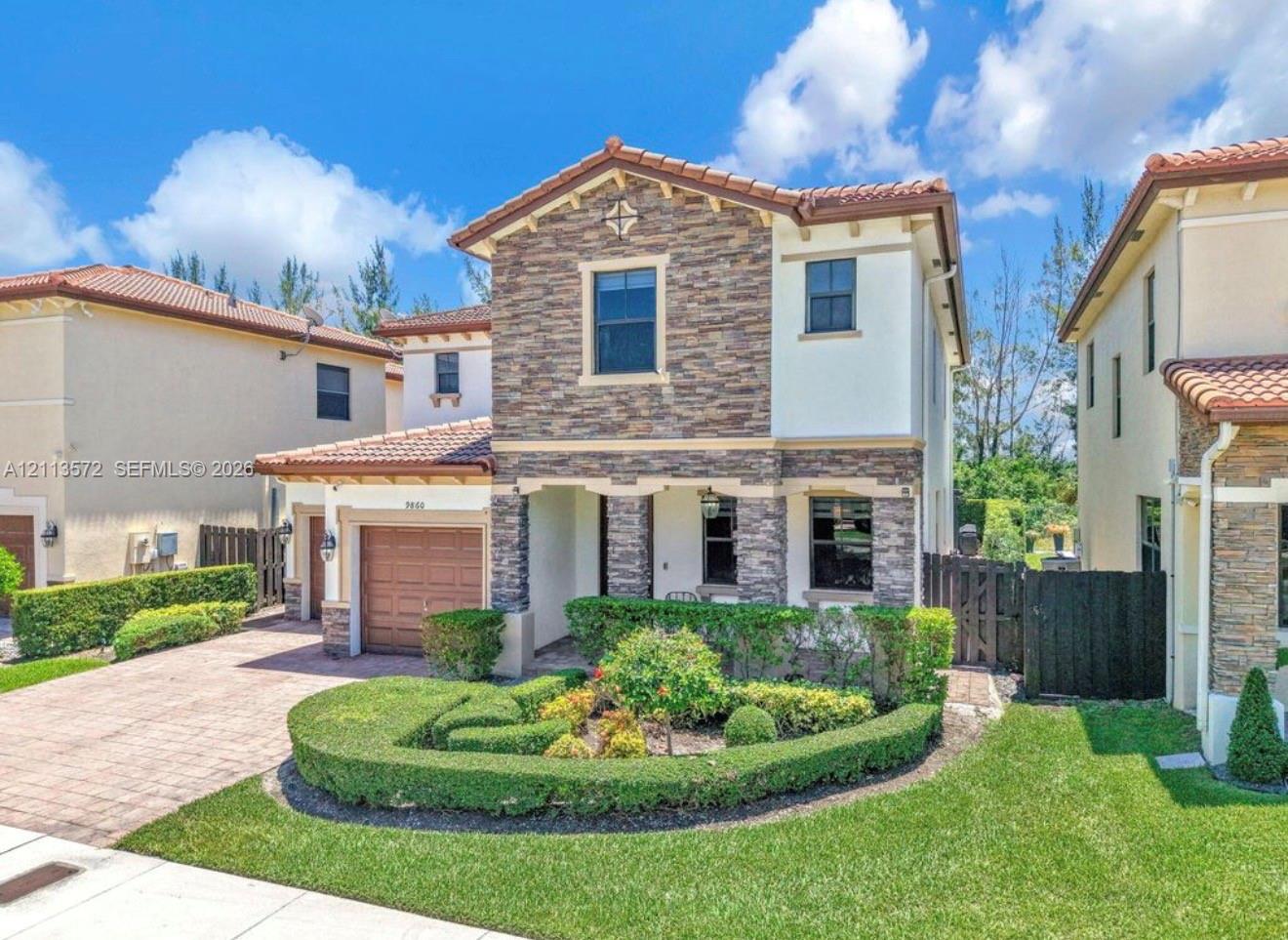 Two-story residence featuring a tile roof, decorative stone veneer faade, manicured landscaping, and a paved driveway
