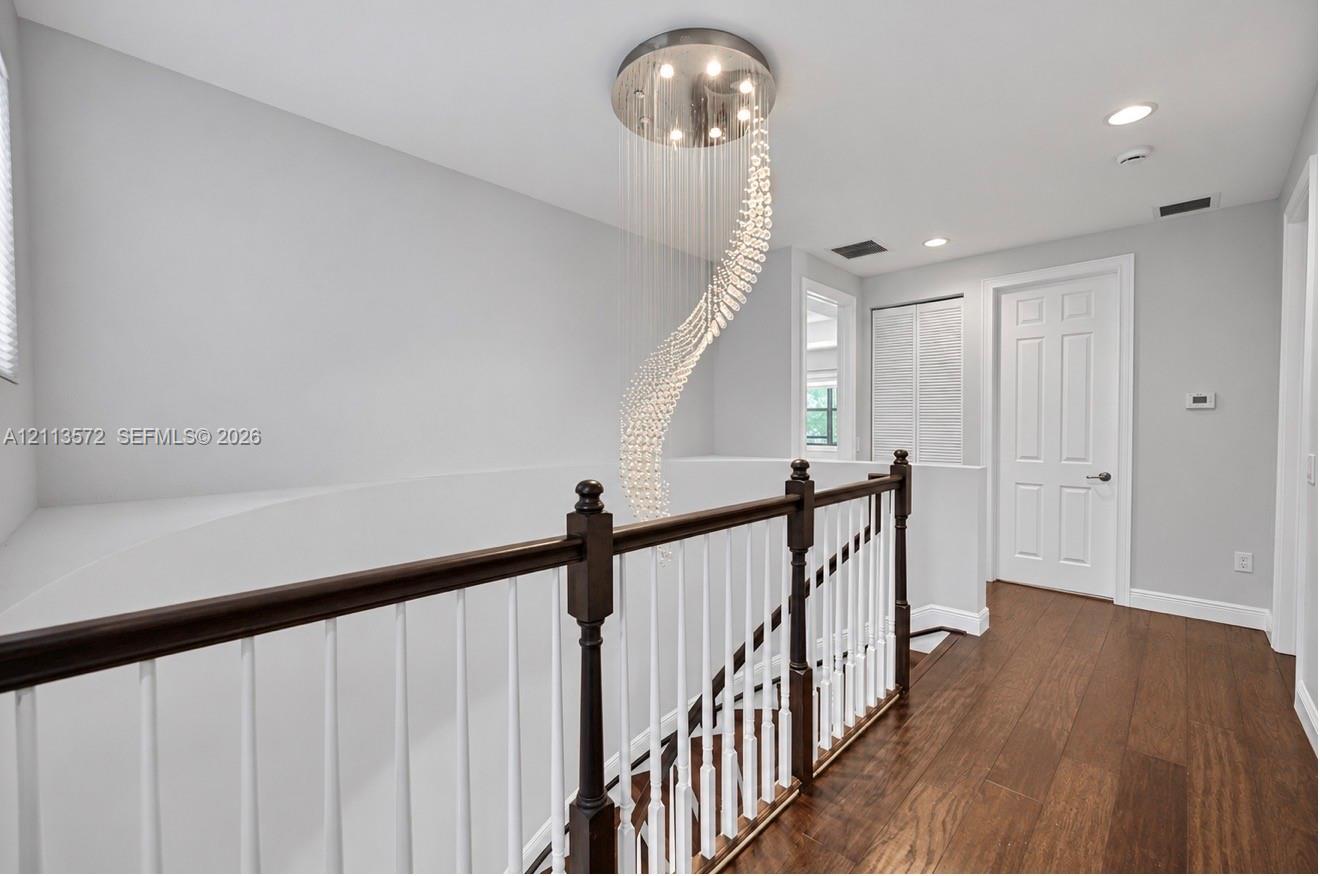 Spiral crystal chandelier with recessed ceiling lighting, wood-finish flooring, and a two-tone railing featuring a dark wood handrail and white balusters