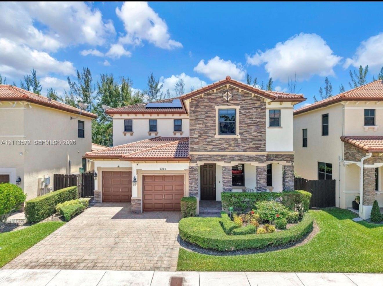 Two-story exterior featuring a stone facade, tile roof, dual-car garage, solar panels, and a paved driveway