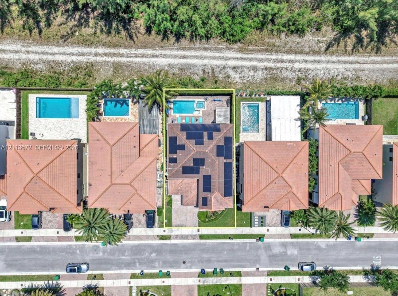 Aerial perspective of property featuring a tile roof with integrated solar panels, private swimming pool, spa, and paved rear patio
