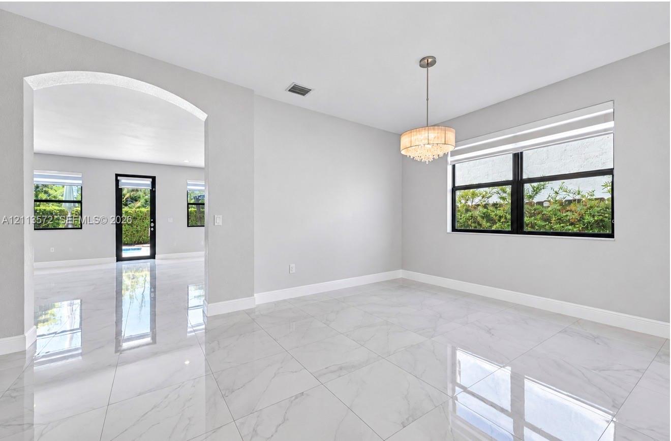 Large-format tile flooring with polished finish, arched architectural entry, multi-tiered crystal drum chandelier, and black-framed window casings