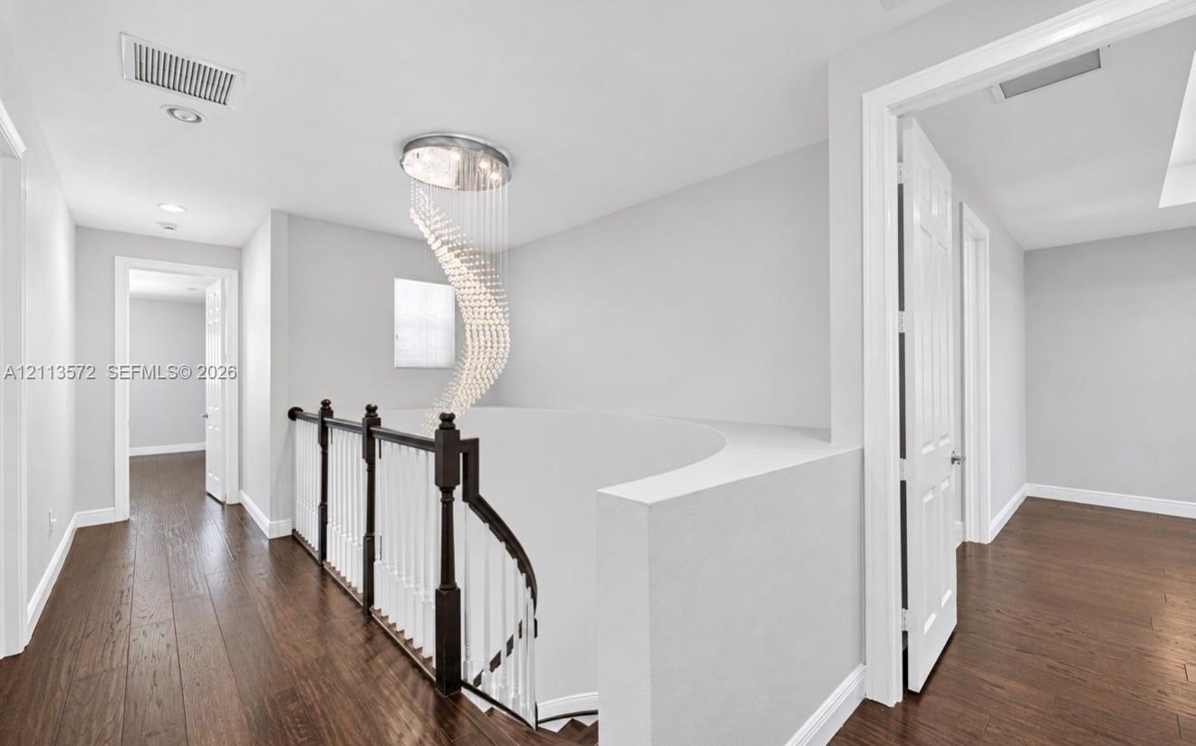 Spiral crystal chandelier, wood-finish flooring, and curved staircase railing featuring dark wood handrails with white balusters