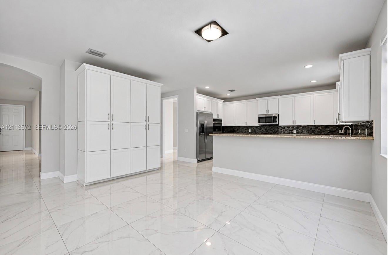 Kitchen featuring white shaker-style cabinetry, a stone-patterned breakfast bar, stainless steel appliances, and large-format porcelain tile flooring