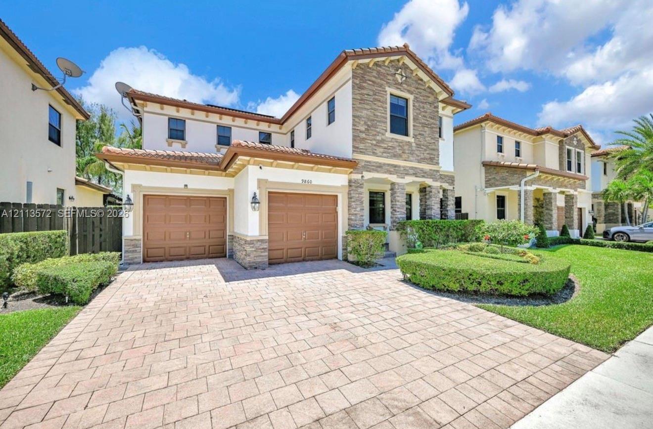 Two-story residence featuring a stone veneer facade, paver driveway, two-car garage, and manicured landscaping