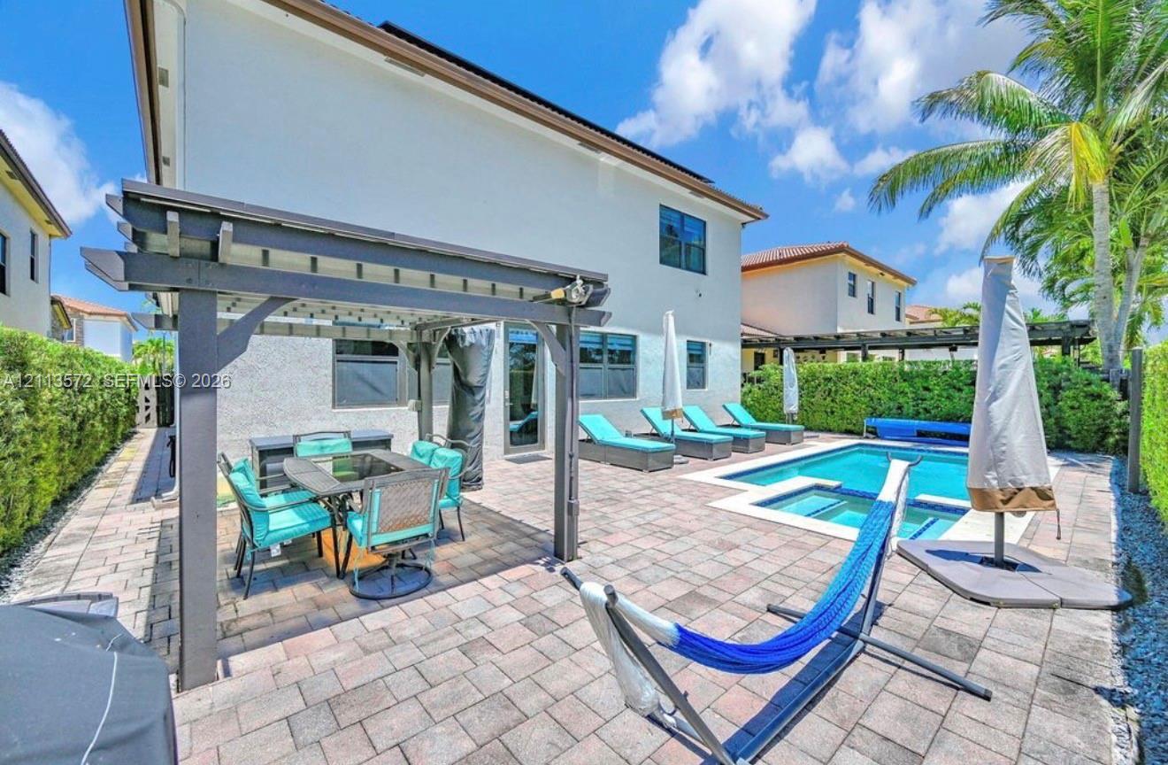 Outdoor living space featuring a paved stone patio, covered pergola, in-ground swimming pool, integrated spa, and perimeter privacy hedges