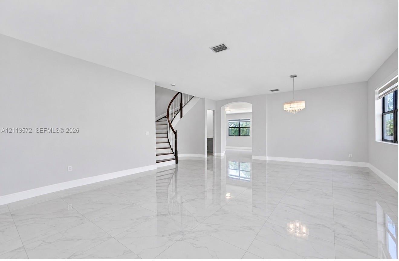 Open-concept interior featuring large-format polished stone-finish flooring, a curved staircase with a dark wood handrail, an arched entryway, and a tiered drum chandelier