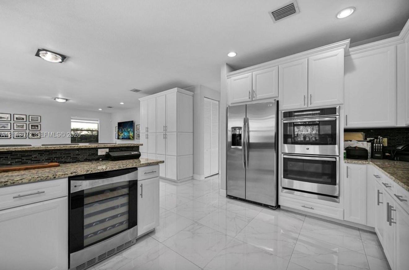 Kitchen featuring white shaker-style cabinetry, stainless steel side-by-side refrigerator, built-in double wall oven, integrated wine refrigerator, and stone countertops