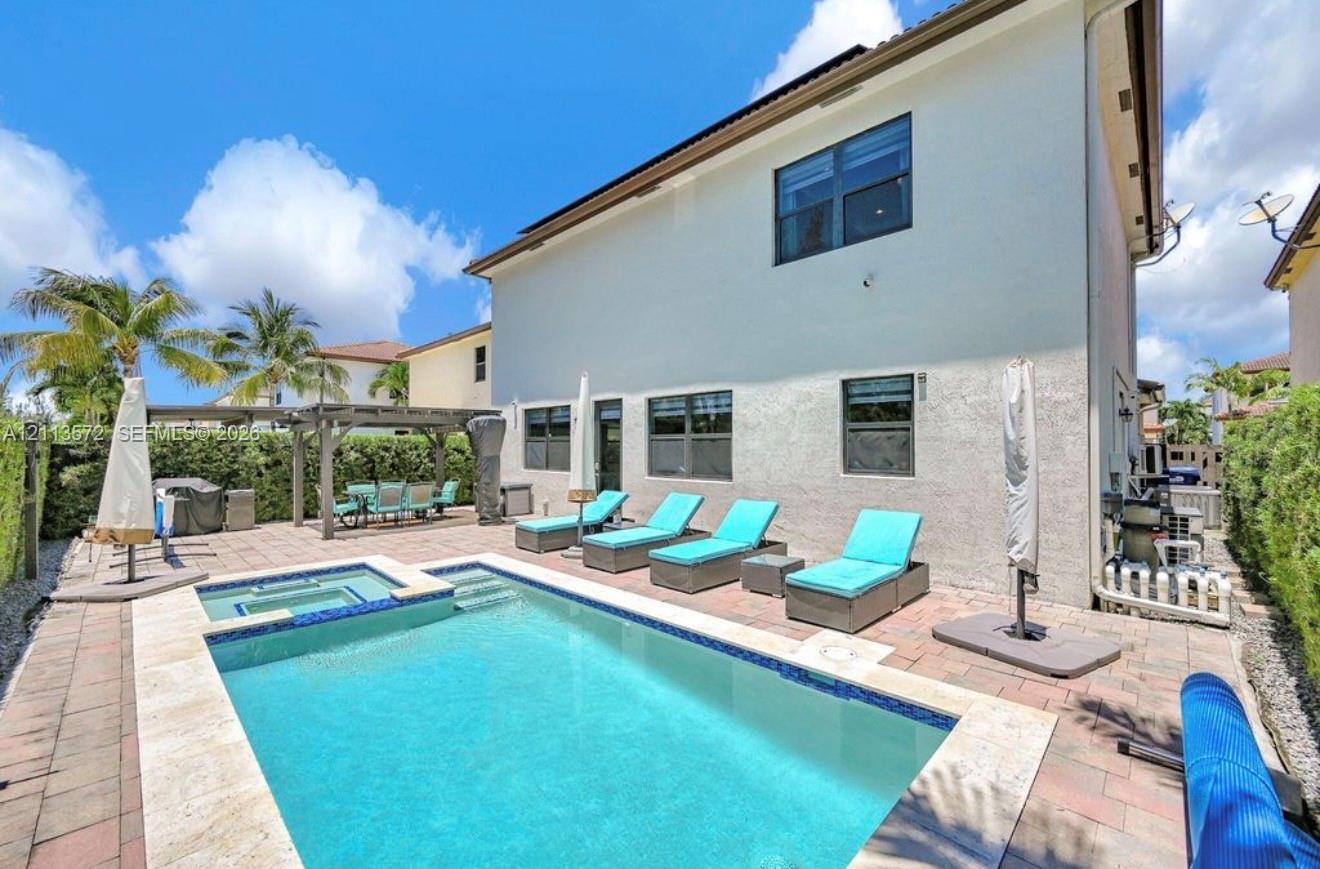 In-ground pool with integrated spa, stone-paver pool deck, and wood-framed pergola