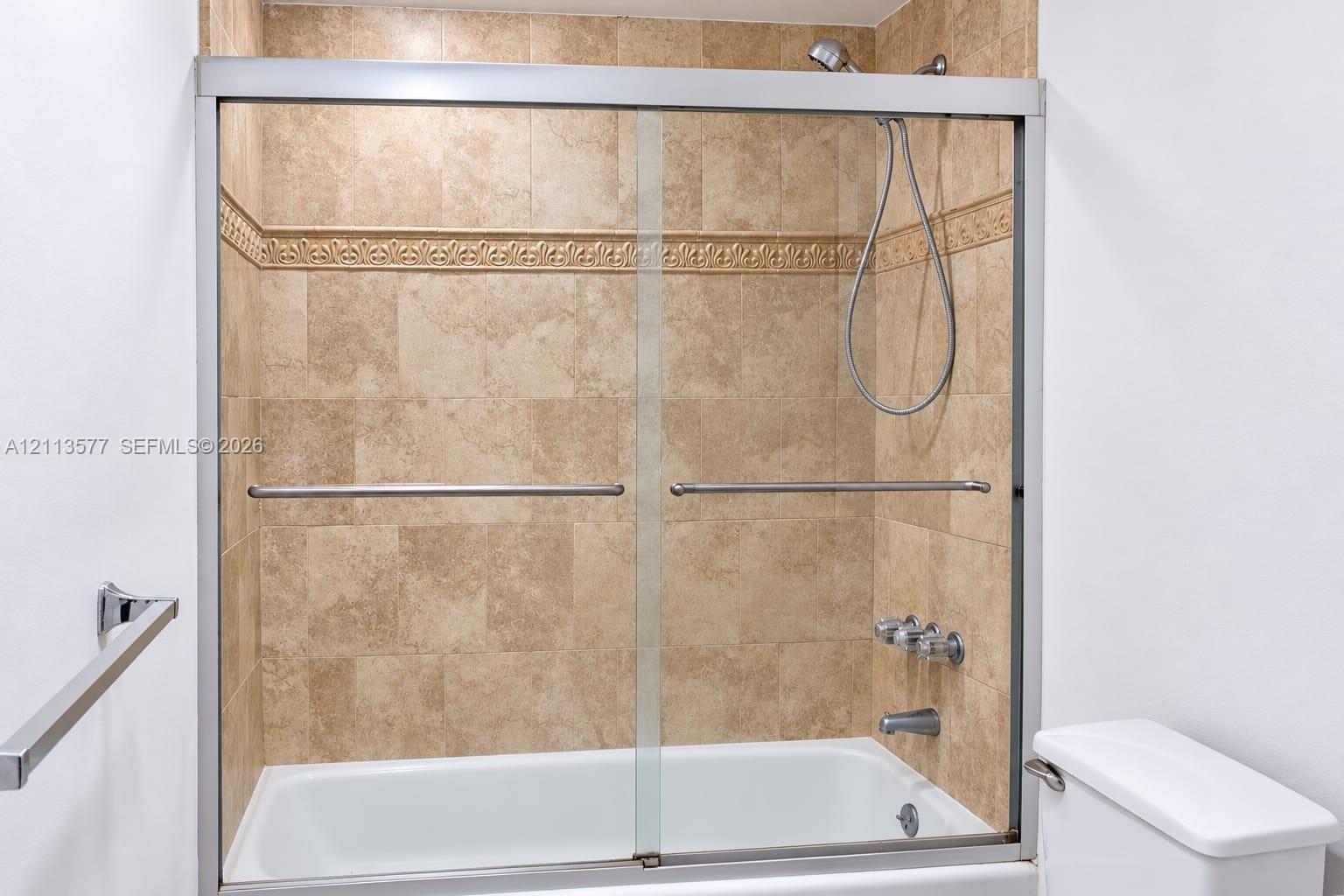 Bathtub and shower combination featuring a glass sliding enclosure, floor-to-ceiling tile surround, decorative tile inlay, and chrome finish hardware