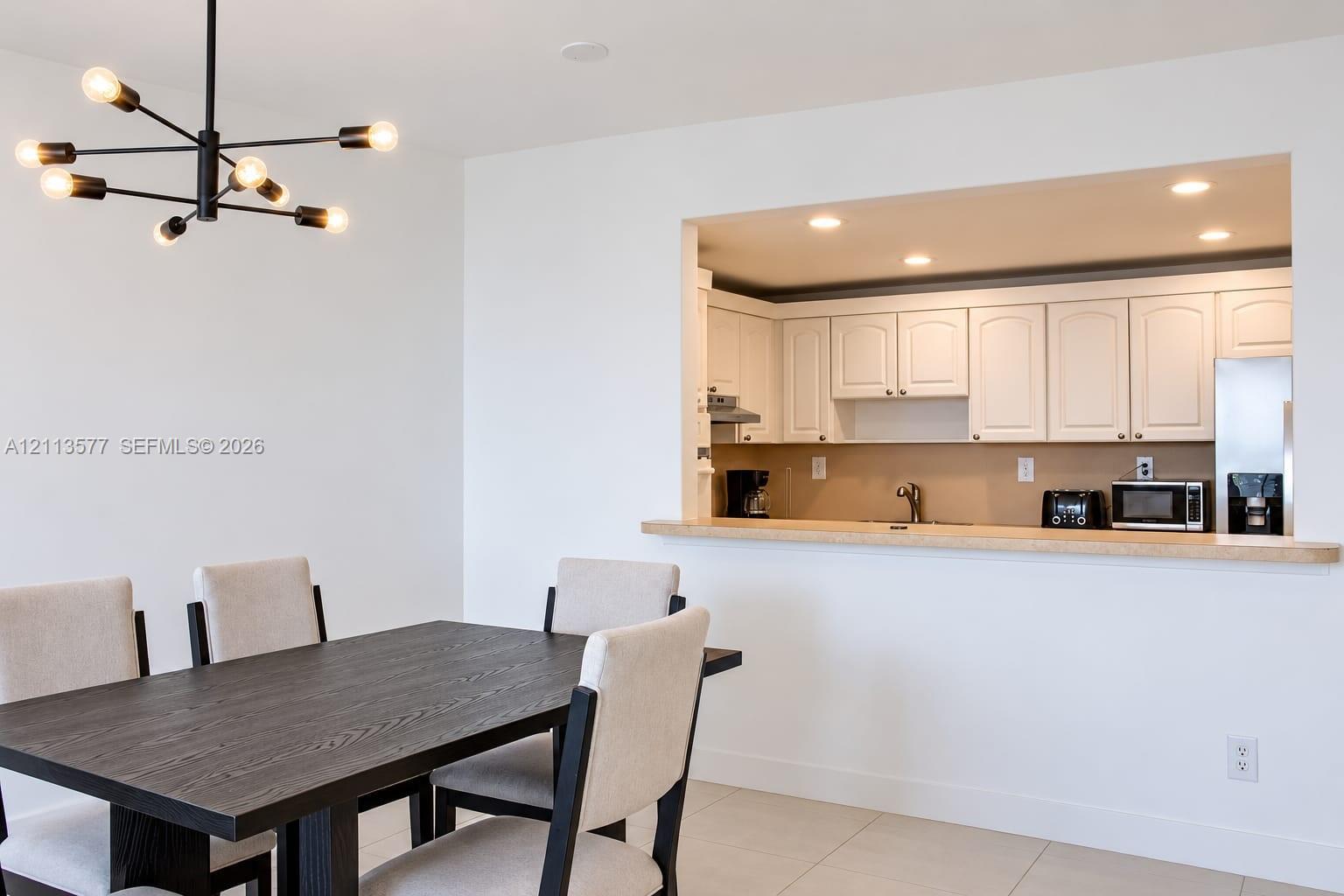 Modern black metal sputnik chandelier, white cabinetry, solid-surface breakfast bar, recessed lighting, and tile flooring Modern black metal sputnik chandelier, white cabinetry, solid-surface breakfast bar, recessed lighting, and tile flooring