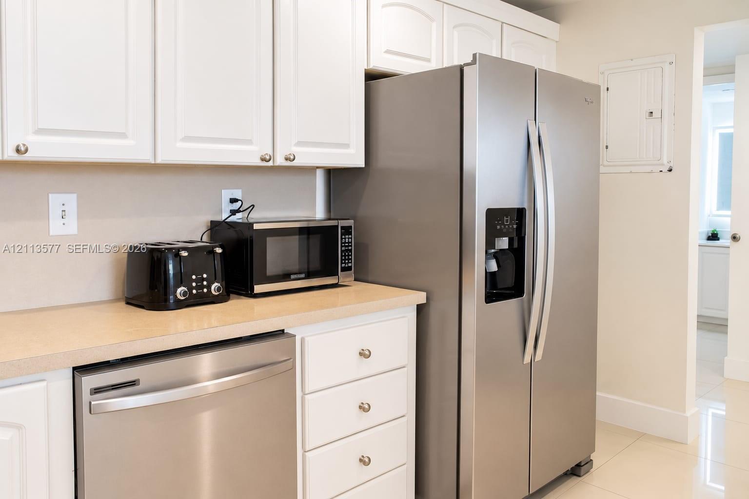 Kitchen featuring white cabinetry, neutral-toned countertops, and stainless steel appliances including a side-by-side refrigerator and dishwasher Kitchen featuring white cabinetry, neutral-toned countertops, and stainless steel appliances including a side-by-side refrigerator and dishwasher