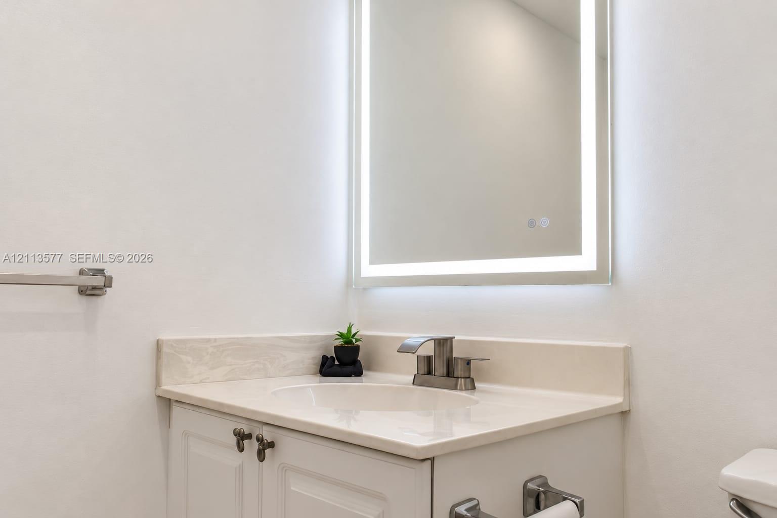 Built-in vanity with integrated countertop and sink, brushed metallic faucet, and wall-mounted illuminated mirror
