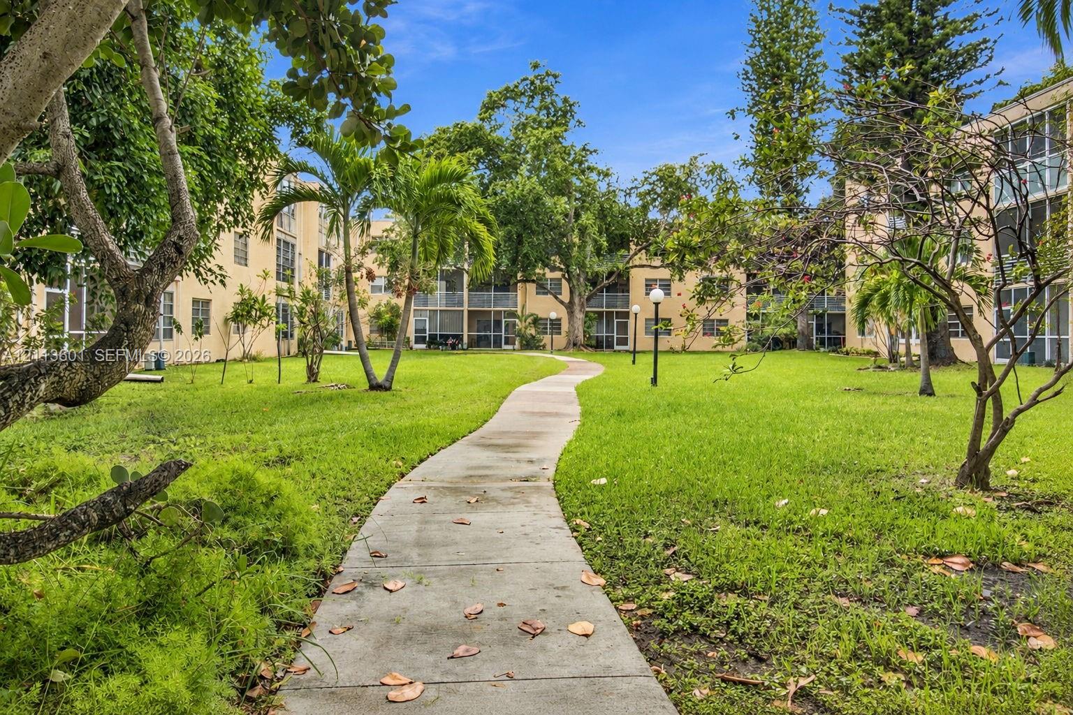 Expansive common grounds featuring a concrete walking path, mature palm trees, established foliage, and residential structures with screened-in enclosures
