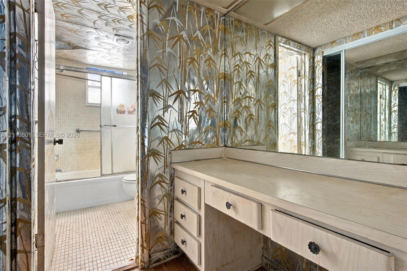 Built-in light-colored wood vanity featuring multiple storage drawers, full-width wall mirror, and metallic patterned wall covering