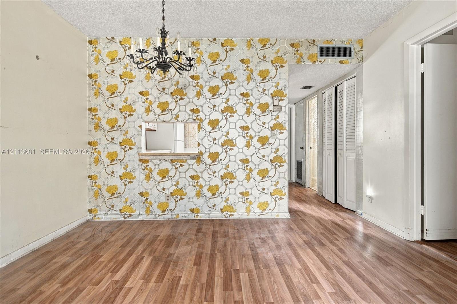 Interior space featuring wood-finish flooring, a decorative floral-patterned accent wall, a traditional multi-arm chandelier, and louvered closet doors