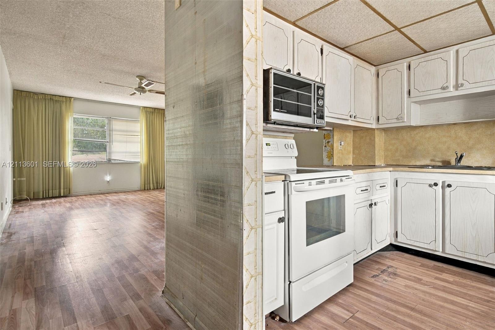 Kitchen featuring white paneled cabinetry, a built-in microwave, a white freestanding range, and wood-finish flooring