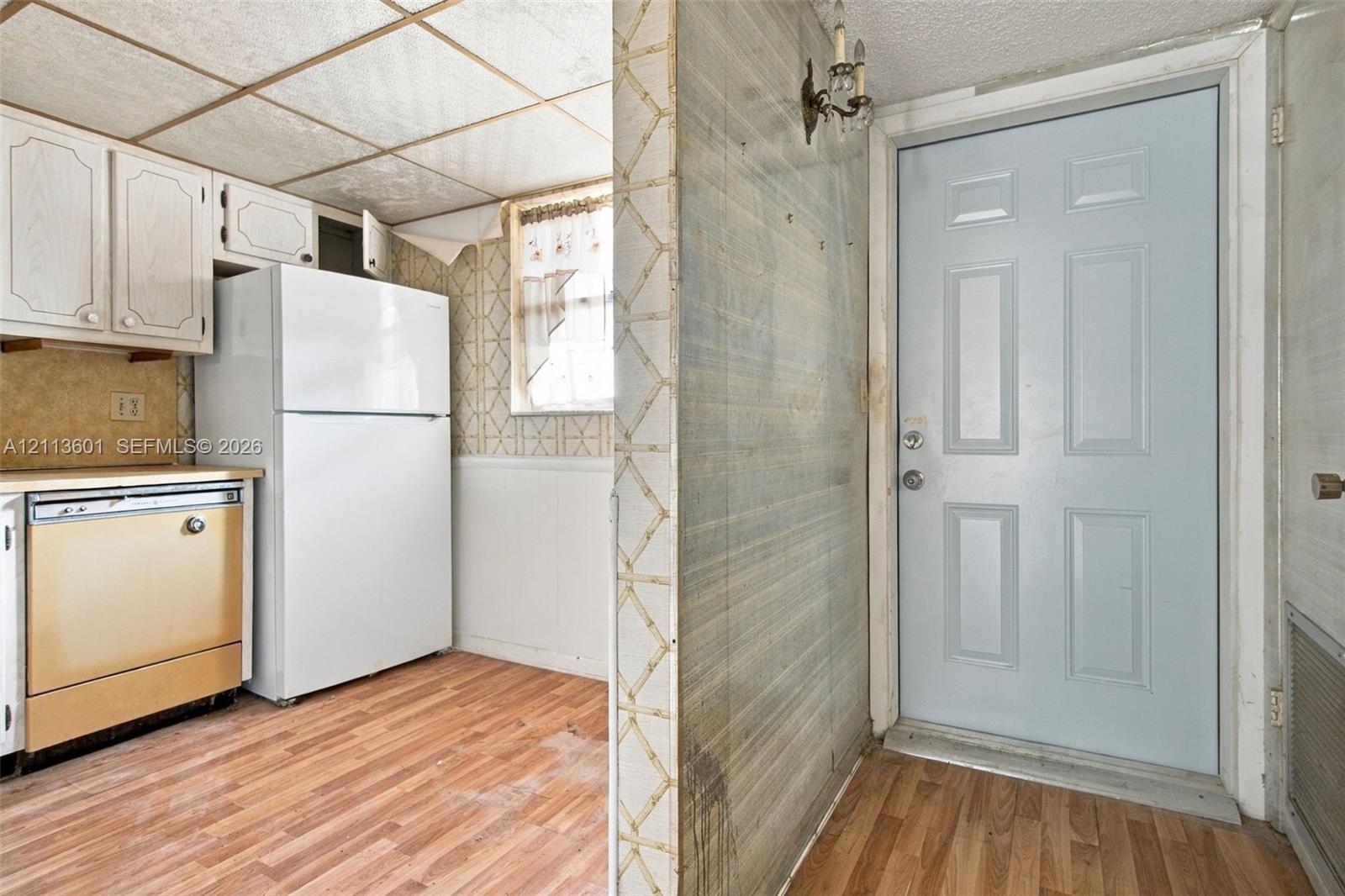 Kitchen area featuring white cabinetry, wood-finish flooring, a window, wall-mounted light fixture, and an exterior door with six panels