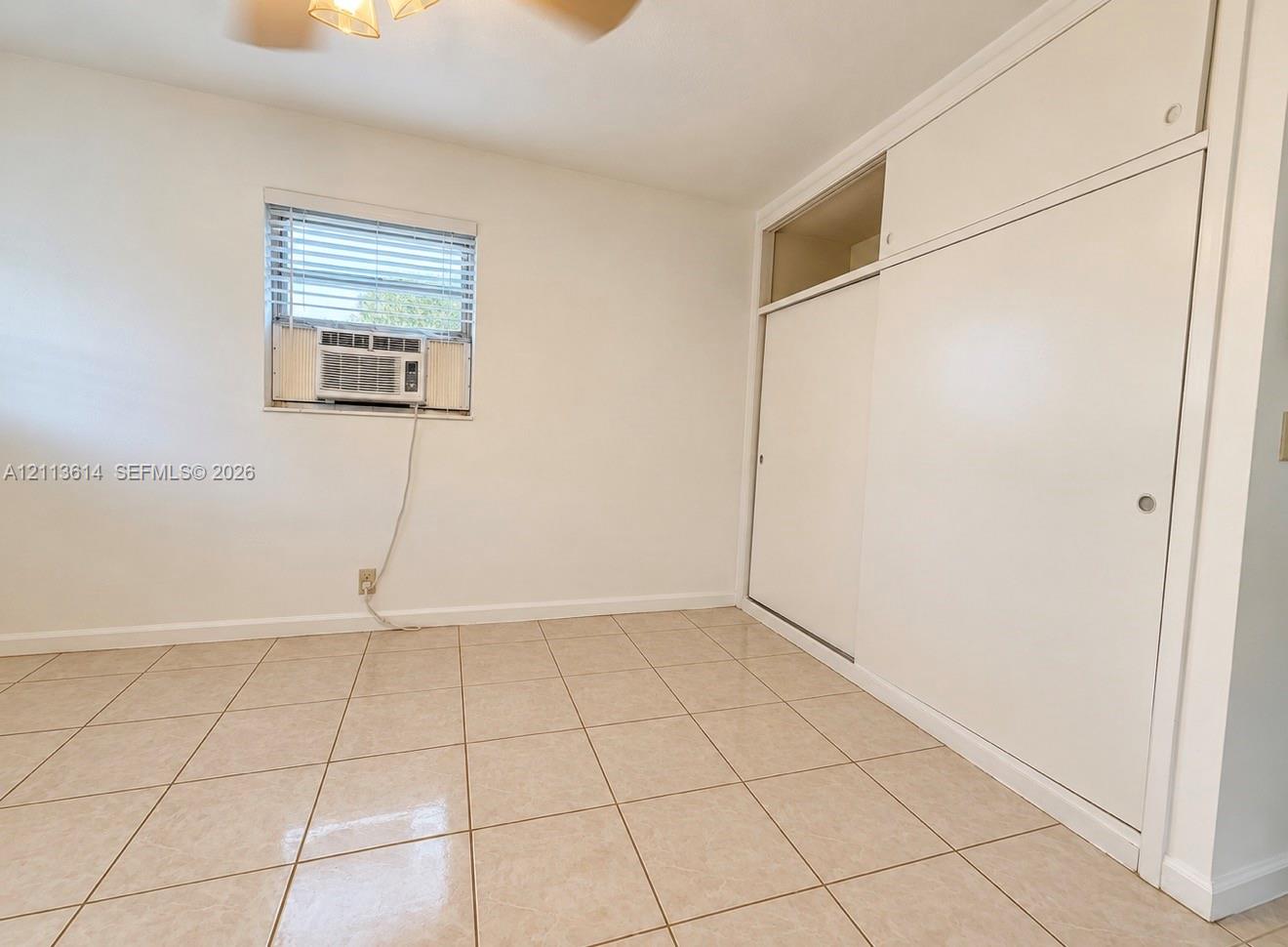 Interior room featuring neutral tile flooring, built-in floor-to-ceiling closet cabinetry, and a window with integrated blinds