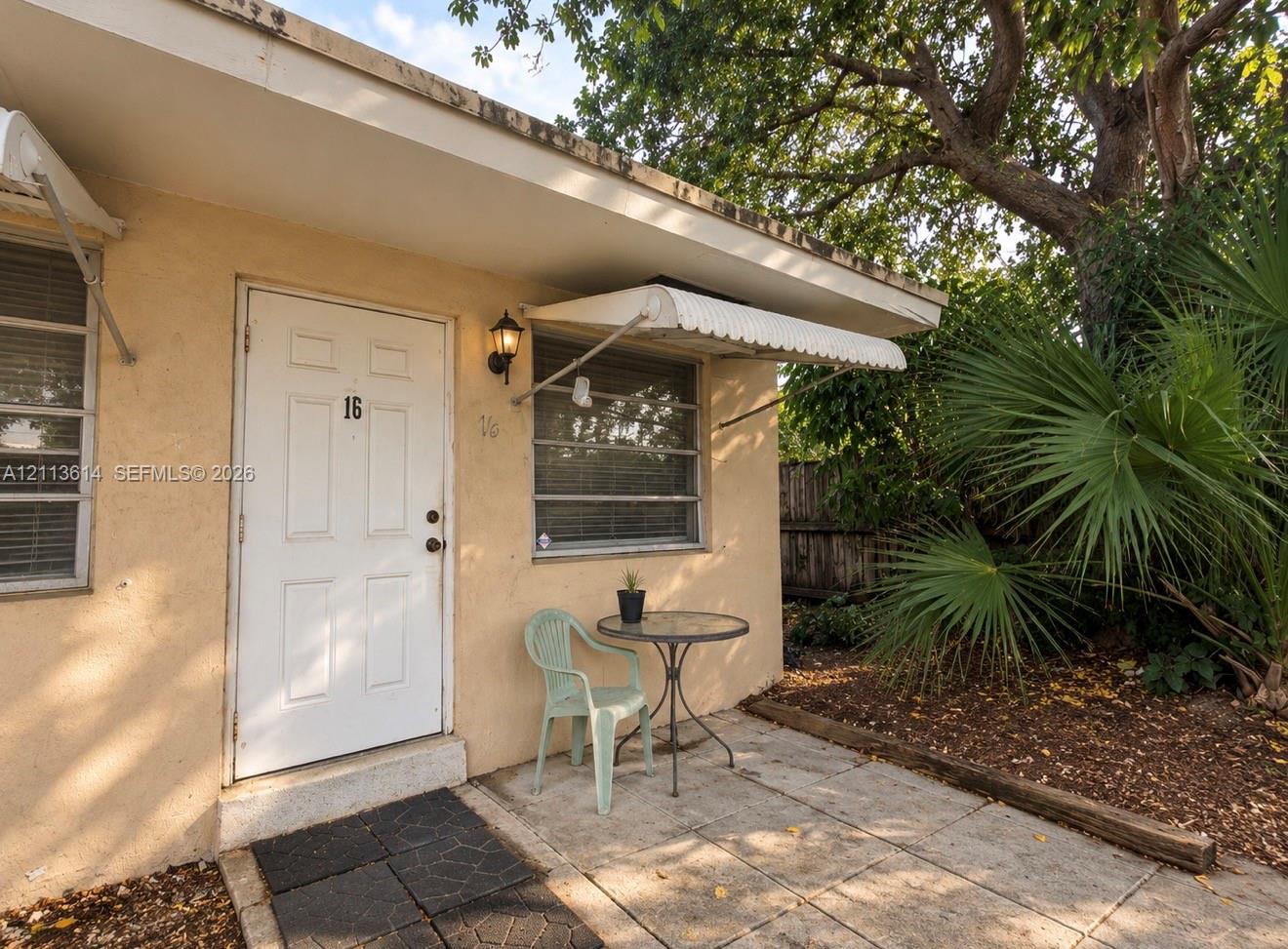 Stucco exterior featuring a paved stone patio, metal window awnings, wall-mounted lantern lighting, and aluminum-frame windows