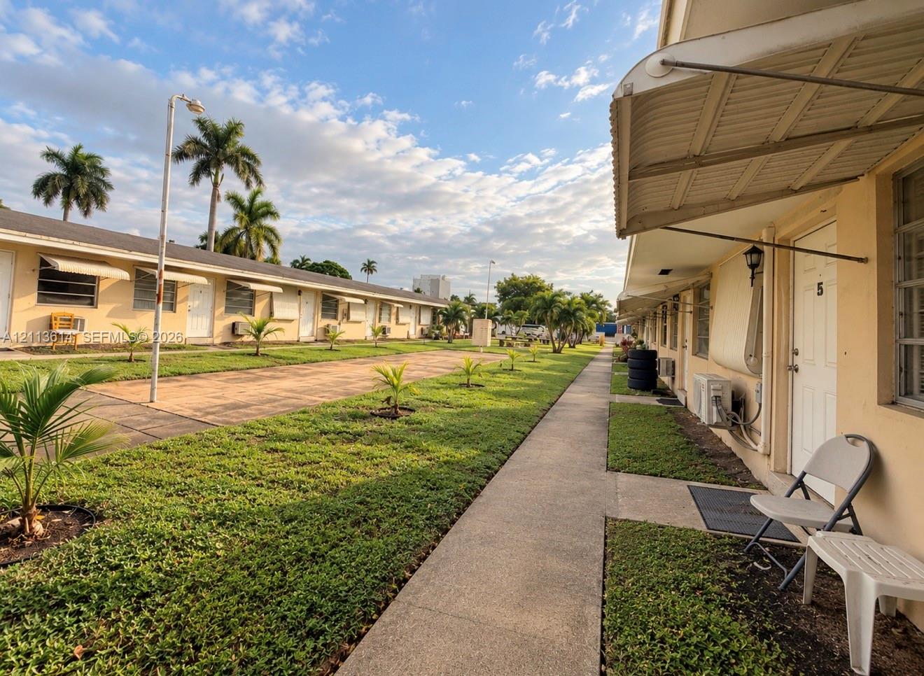 Single-story exterior featuring metal awnings, stucco siding, concrete walkways, and manicured landscaping with palms
