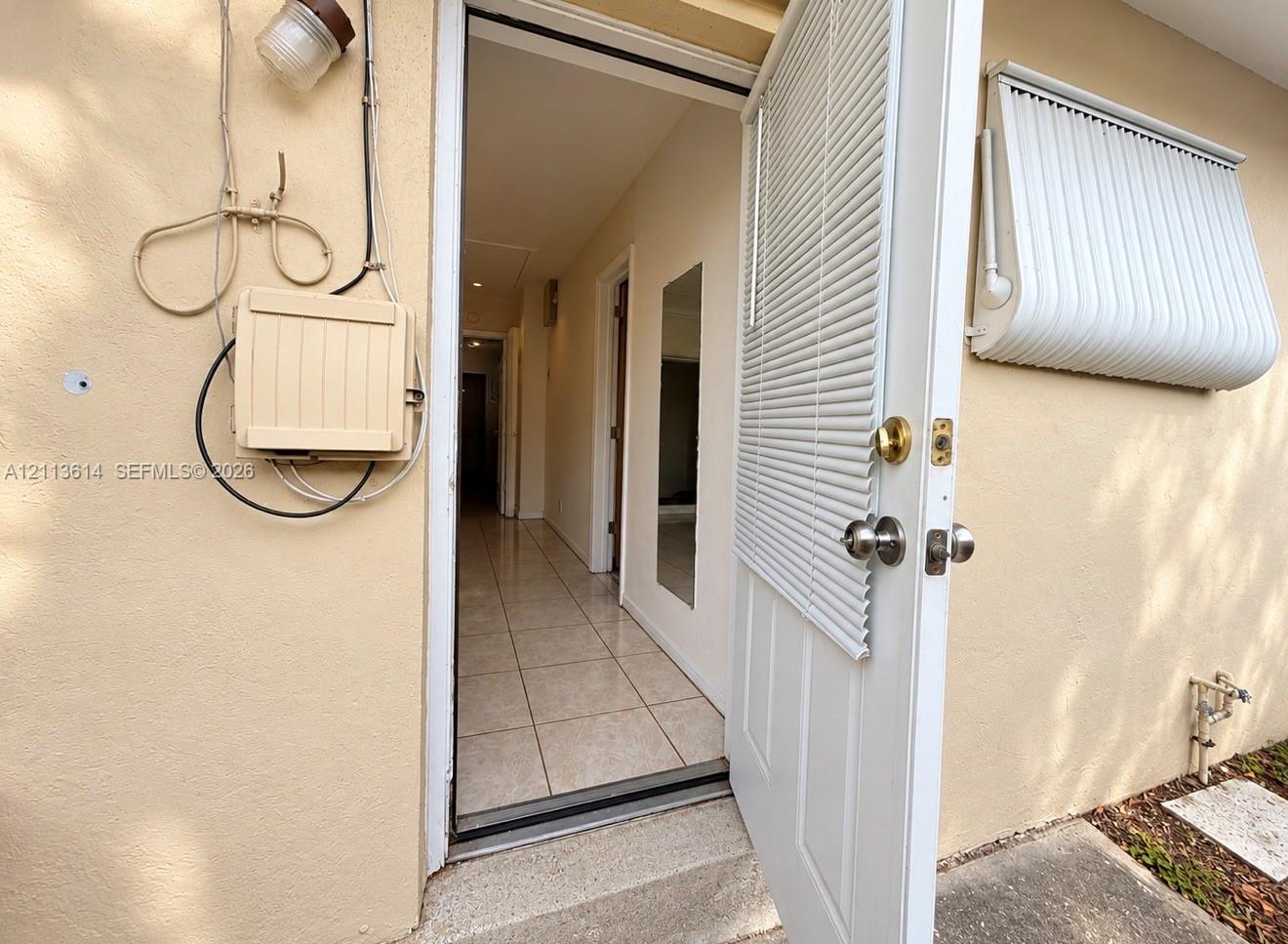 Exterior entry featuring an integrated door blind, a metal window awning, and tile flooring