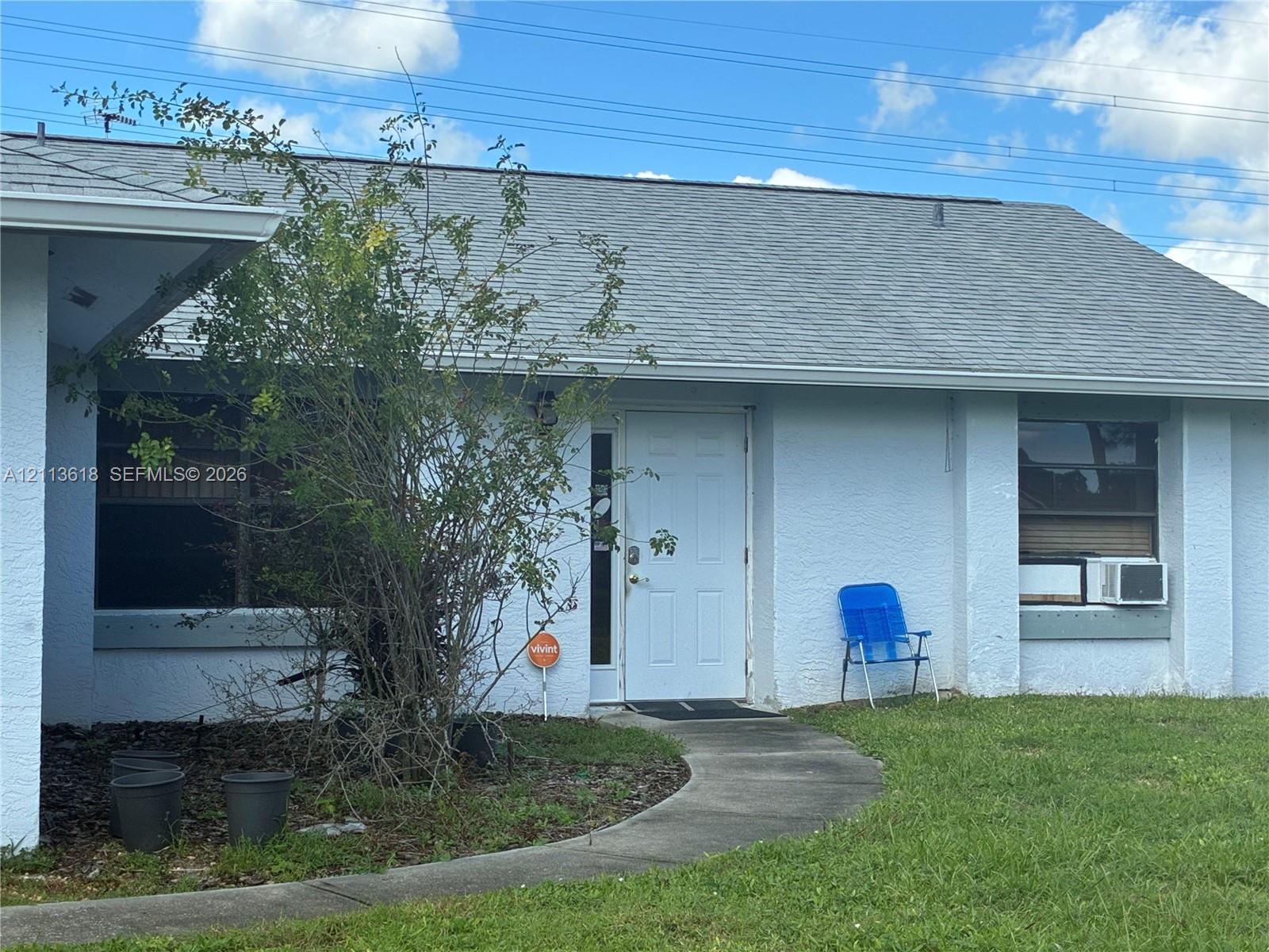 Single-story exterior featuring light-colored textured masonry, a gabled roof with asphalt shingles, and a paved walkway