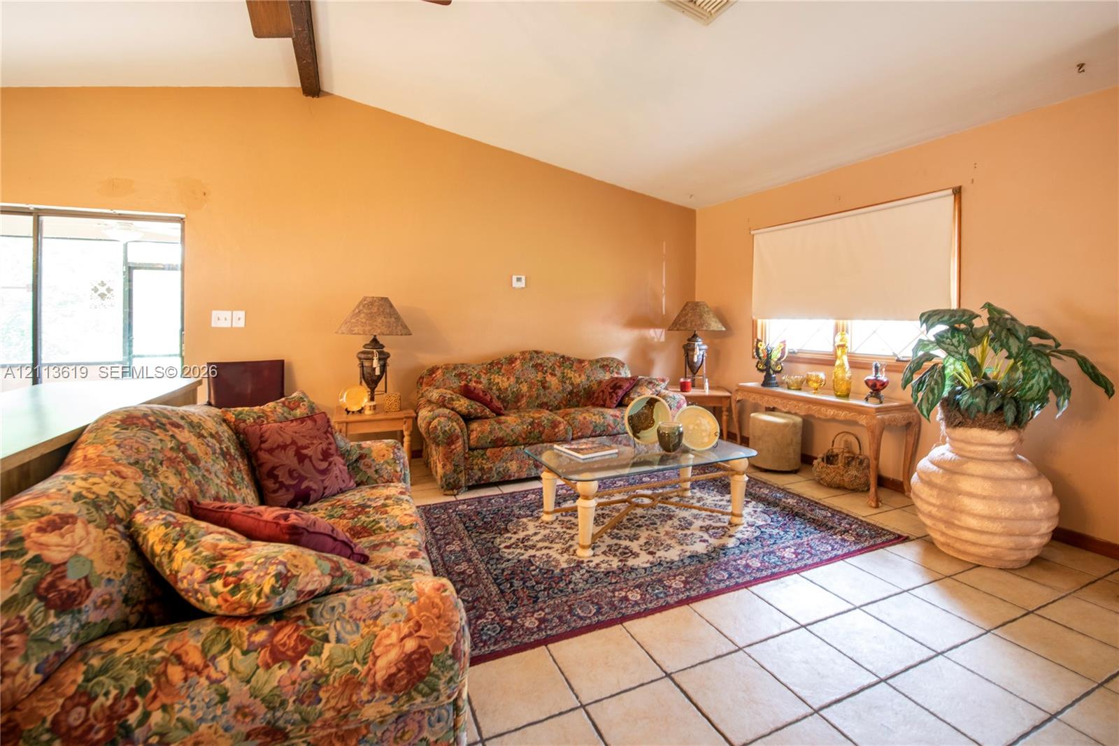 Vaulted ceiling with exposed wood beam, large-format tile flooring, and oversized window with neutral roller shade