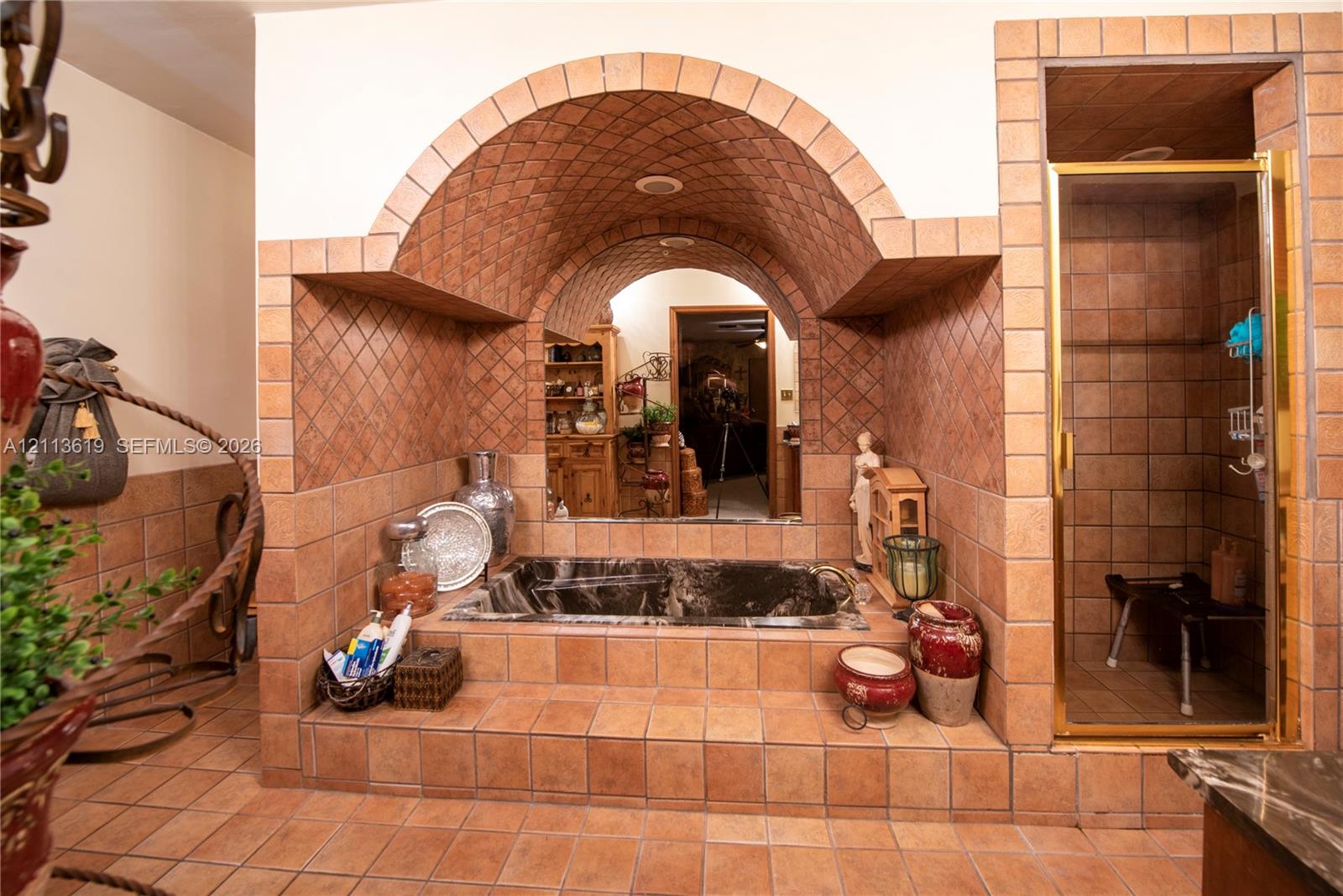 Custom tiled alcove featuring a barrel-vaulted ceiling, built-in soaking tub, integrated vanity mirror, and an enclosed shower with gold-tone framing