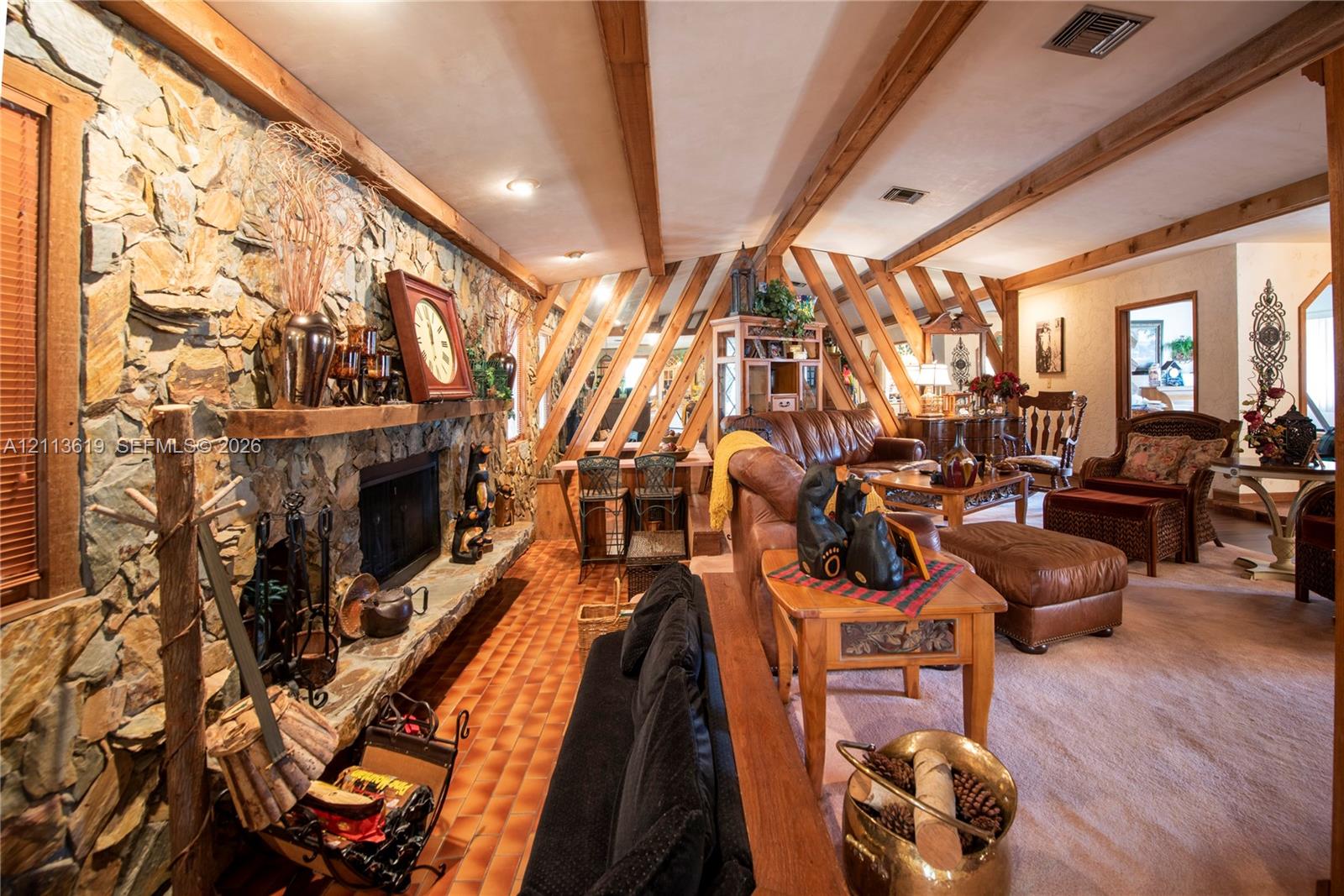 Floor-to-ceiling stone fireplace with a thick timber mantel, exposed wooden ceiling beams, diagonal wood wall accents, and tile flooring Floor-to-ceiling stone fireplace with a thick timber mantel, exposed wooden ceiling beams, diagonal wood wall accents, and tile flooring