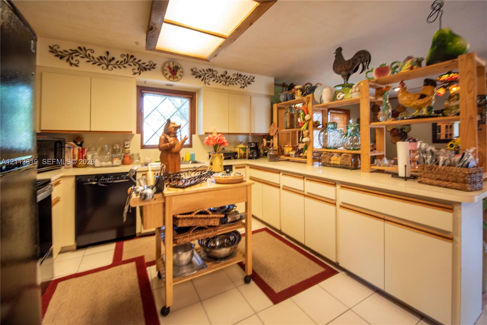 Kitchen featuring ample flat-panel cabinetry, light-toned countertop surfaces, tile flooring, and a window with diamond-pane glass detailing Kitchen featuring ample flat-panel cabinetry, light-toned countertop surfaces, tile flooring, and a window with diamond-pane glass detailing