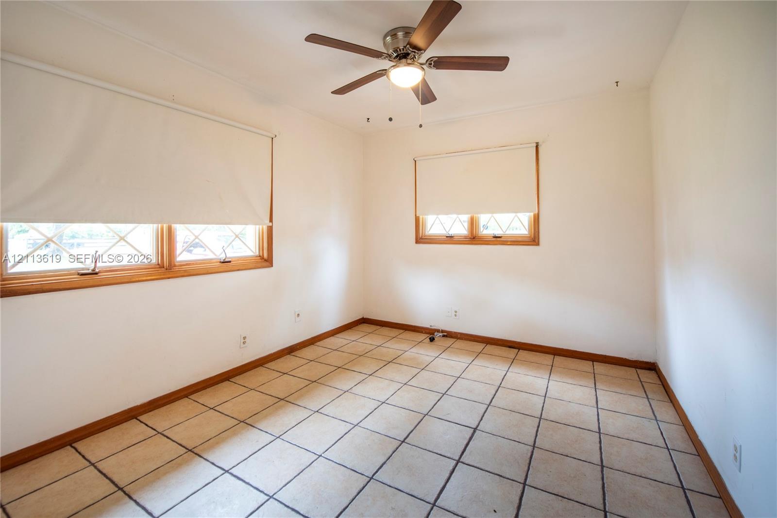 Interior room featuring ceramic tile flooring, two windows with wood frames, and a ceiling-mounted light fixture with a fan