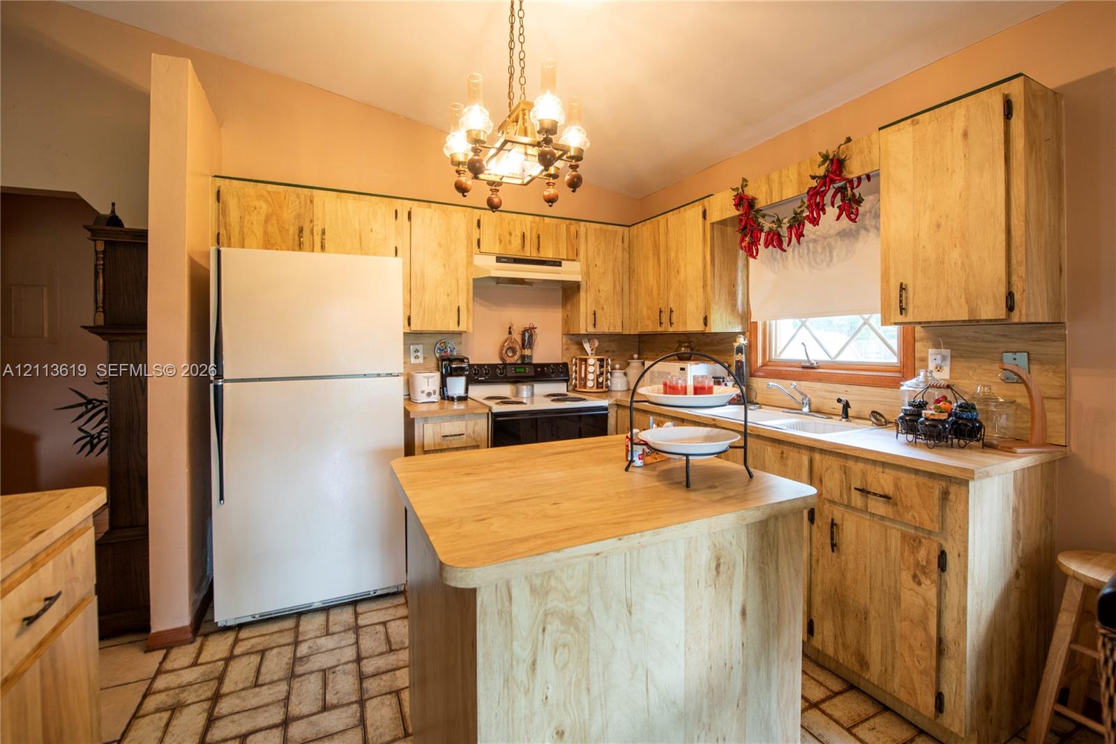 Kitchen featuring light wood cabinetry, a central island with a wood-finish countertop, dual-basin sink, and multi-bulb chandelier