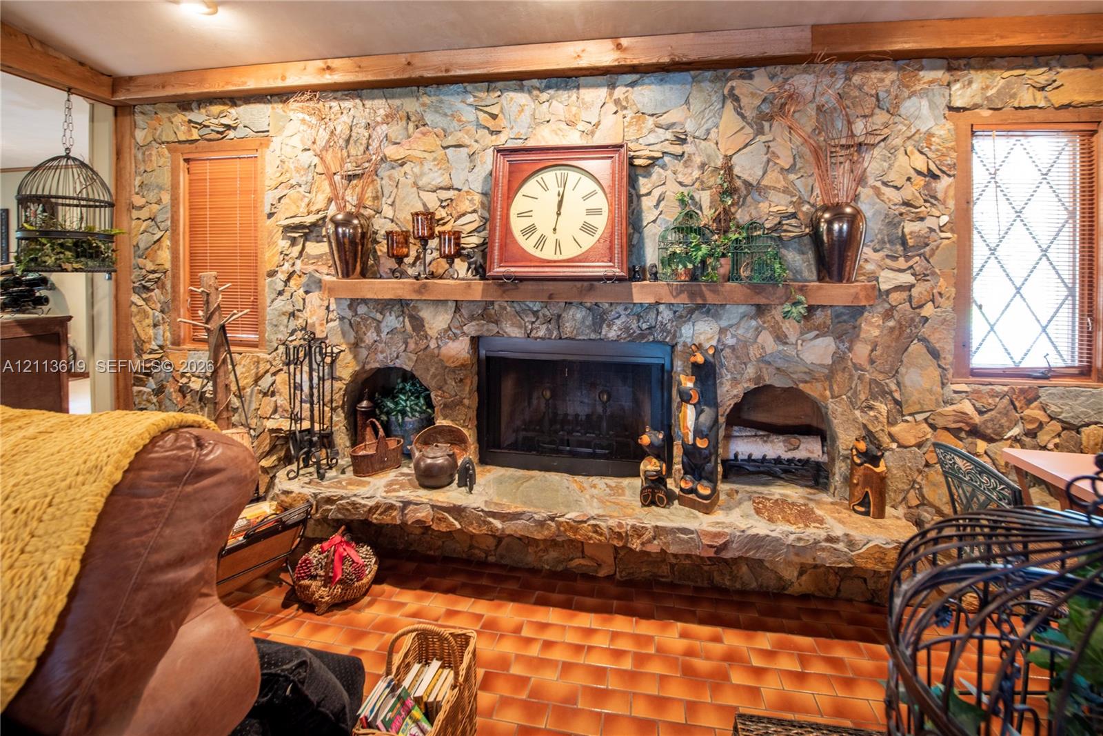 Floor-to-ceiling natural stone fireplace featuring an integrated stone hearth, dual side-arch storage alcoves, a solid timber mantel, and grid-pattern window pane inserts Floor-to-ceiling natural stone fireplace featuring an integrated stone hearth, dual side-arch storage alcoves, a solid timber mantel, and grid-pattern window pane inserts