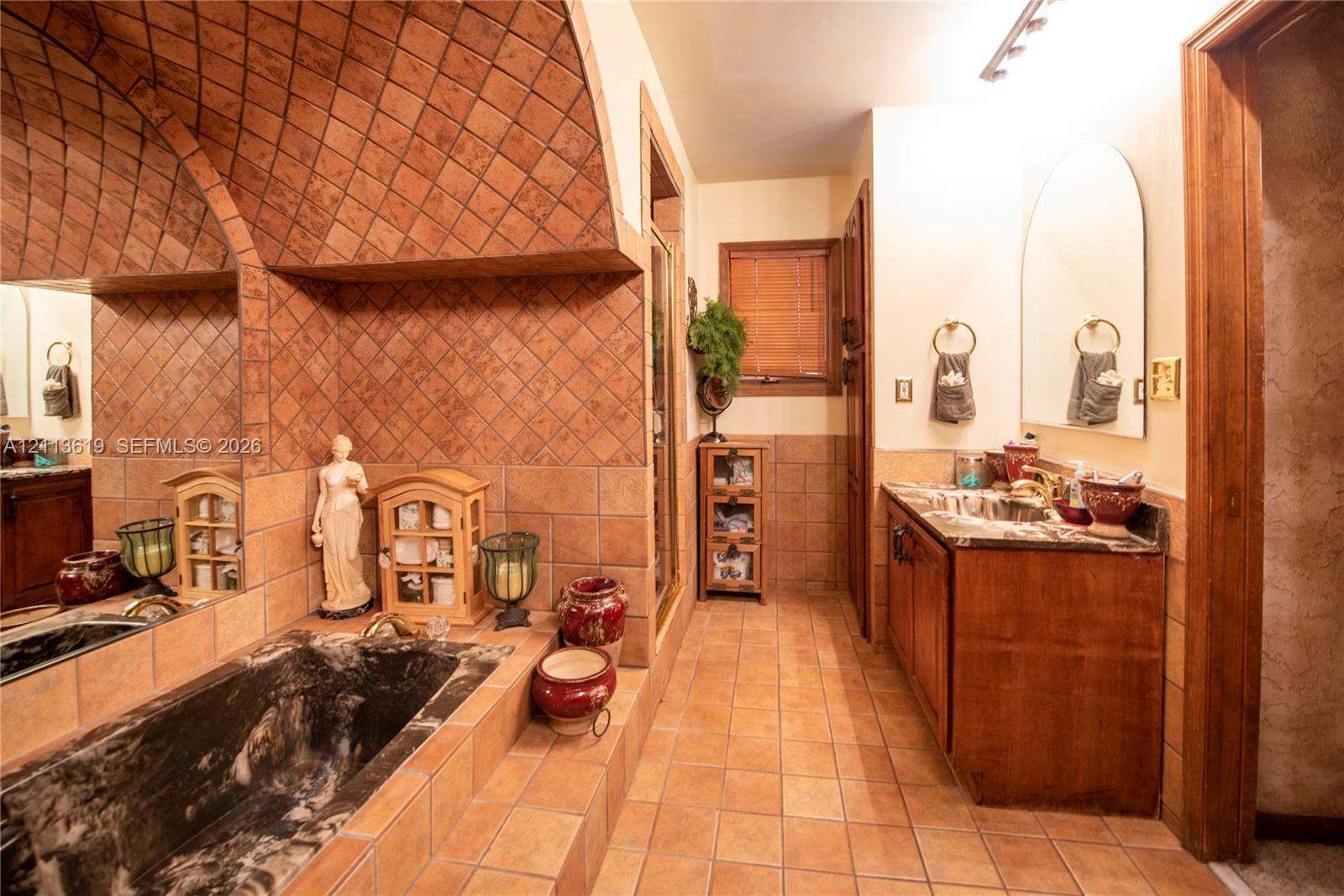 Vaulted barrel-style ceiling with diagonal tile inlay, recessed soaking tub with integrated stone surround, custom wood cabinetry, countertop-mounted sink, and wall-mounted arched mirror