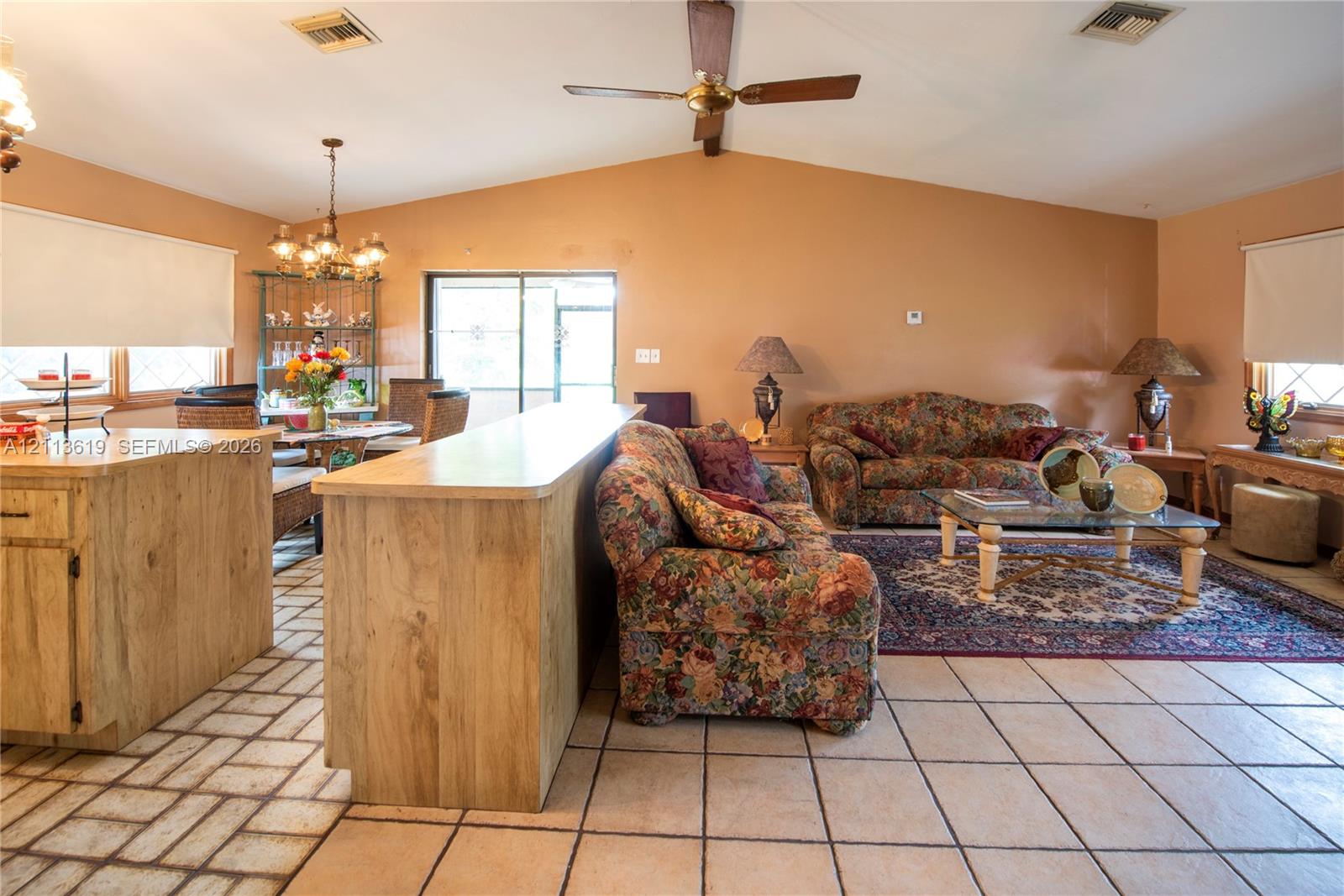 Vaulted ceiling with a centrally mounted ceiling fan, tile flooring, and a built-in peninsula cabinet with a flat-surface countertop