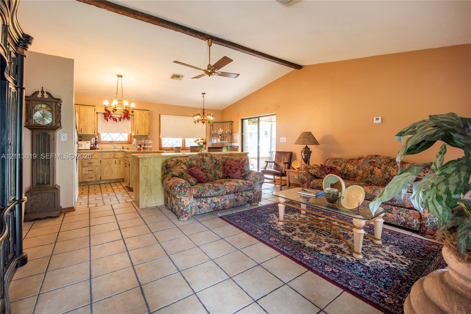 Open-concept interior featuring vaulted ceilings with exposed wood beams, ceramic tile flooring, and a kitchen island with stone-finish cabinetry