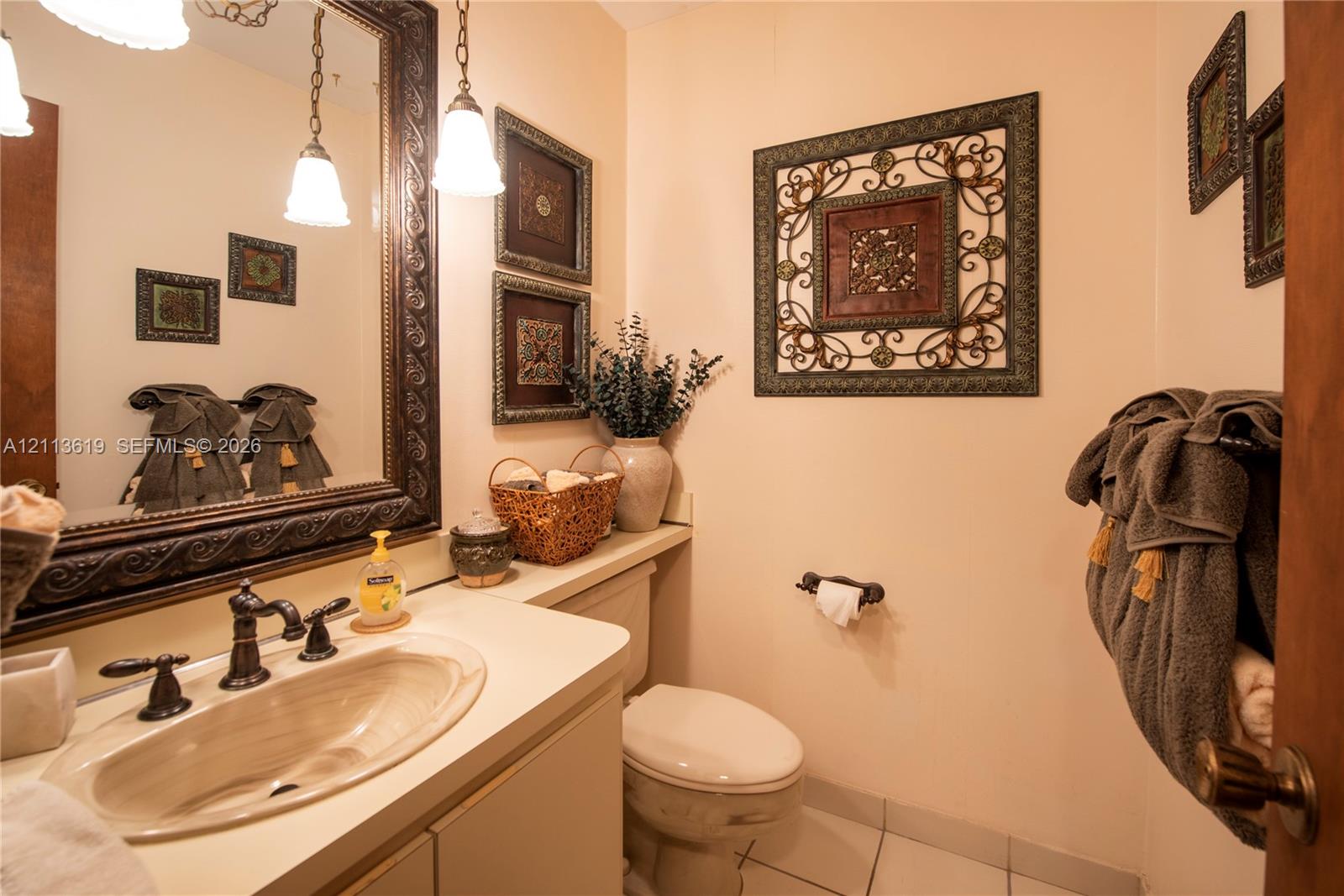 Solid surface vanity countertop with an integrated oval sink, ornate dark-finish framed wall mirror, dual pendant lighting, and neutral tile flooring