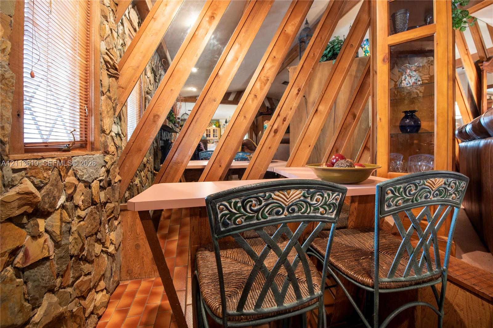Exposed wood beam ceiling supports, natural stone wall masonry, built-in glass-paneled cabinetry, and terracotta tile flooring